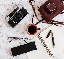 escritorio plano de oficina con vista superior. espacio de trabajo de escritorio con cámara retro, diario, bolígrafo, gafas, estuche, taza de café sobre fondo blanco. foto