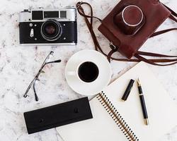 escritorio plano de oficina con vista superior. espacio de trabajo de escritorio con cámara retro, diario, bolígrafo, gafas, estuche, taza de café sobre fondo blanco. foto