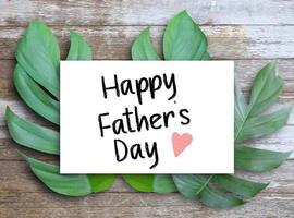 letras felices del día del padre escritas en papel blanco colocadas en hojas y mesa de madera foto