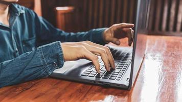Man hand working using laptop at home while sitting at a wooden desk male hand typing on notebook keyboard photo