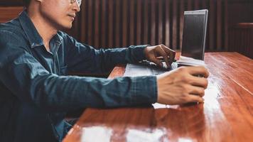 un joven con anteojos usando una computadora portátil escribiendo en un teclado, escribiendo correos electrónicos o trabajando en línea en una computadora en su sala de estar. foto