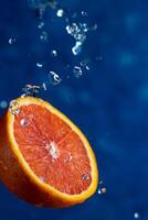 Half an orange falls on a blue background with drops of water photo