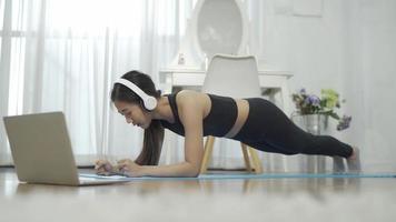 sportieve jonge vrouw die rekoefeningen doet tijdens het online kijken naar fitnessvideo op laptop thuis. gezond levensstijlconcept