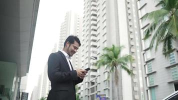 negócios um jovem de camisa xadrez está navegando em seu smartphone na cidade. sorrindo bonito, confiante masculino se comunicando em um smartphone em um fundo de prédio urbano. video