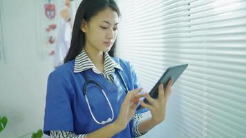 Asian Doctor female using digital tablet computer app standing in hospital office. Young woman professional doctor holding touchscreen pad device in clinic. Online healthcare medical tech concept