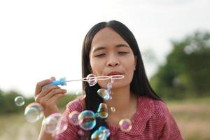 Asian woman blowing soap bubbles every green grass background photo