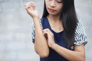 mujer rascándose el brazo por picazón en un fondo gris claro. la causa de la picazón en la piel incluye picaduras de insectos concepto de cuidado de la salud de la piel. foto