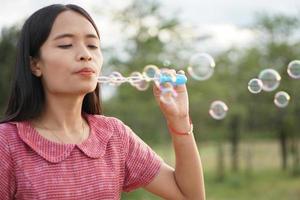 Asian woman blowing soap bubbles every green grass background photo