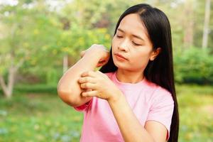 Woman scratching arm from itching on light gray background. Cause of itchy skin include insect bitesConcept of health care skin. photo