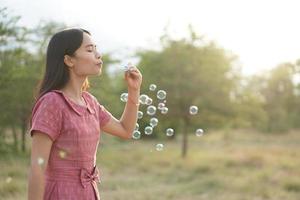 Asian woman blowing soap bubbles every green grass background photo