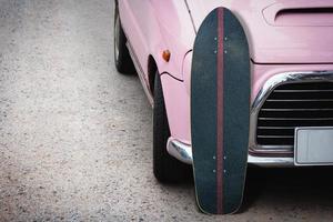 Old surfskate with pink vintage car on road in the parking. photo