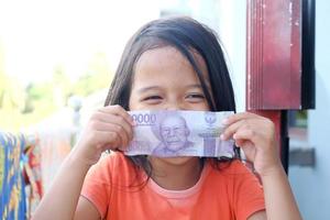 Indonesian little girl covering her mouth with rupiah banknotes photo