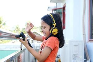 Asian little girl wearing headphones with video call, Happy young girl video calling with friends photo