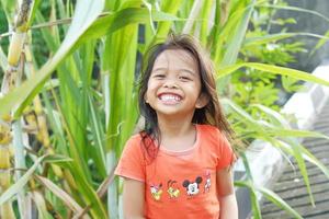 expresión feliz niña indonesia con el pelo suelto en el fondo de la caña de azúcar foto