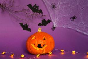 Halloween backgrounds of Jack lantern natural pumpkin, spiders and black bats on a purple background with terrible scenery. Horror and a scary holiday with copy space