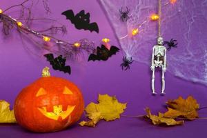 Halloween backgrounds of Jack lantern pumpkin, spider web, skeleton on a rope, spiders and black bats on a purple background with terrible scenery. Horror and a scary holiday with copy space photo