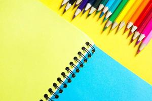 paleta arcoiris de lápices de colores con un cuaderno en espiral sobre un fondo amarillo, maqueta, puesta plana. regreso a la escuela, reclutamiento de estudiantes, artista, lecciones de dibujo. copie el espacio papelería para la creatividad foto