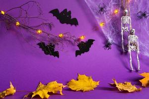 Halloween backgrounds of Jack lantern pumpkin glowing garland, spider web, skeleton on a rope, spiders and black bats on a purple background with dry yellow leaves. Horror and a scary holiday