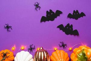 Halloween layout of white, orange and gold pumpkins, spiders and black bats on a purple background with a glowing garland of Jack o Latern. Flat lay horror and a terrible holiday with copy space photo