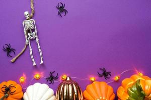 Halloween layout of garland of skeleton on a rope, glowing Jack o Lantern, pumpkins, spiders on a purple background. Flat lay horror and a terrible holiday