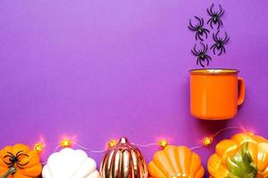 Orange mug on a purple background with terrible Halloween decorations. The concept of the Halloween holiday. Drink, fun, party. Copy space, mock up, flatly photo