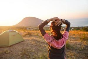 Woman meets the dawn in the mountains, rejoices in the sun. Panoramic view of the mountain and the sea from above. Camping, outdoor activities, sports mountain hiking, family travel. Ayu-Dag, Crimea. photo