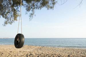 Tire swings hang from trees on the sandy beach. With a background of blue sea and sky with coluds photo