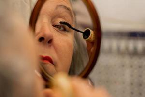 older woman painting her eyelashes in front of a mirror photo