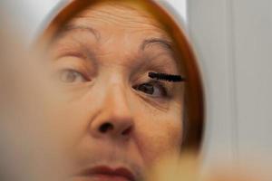 older woman painting her eyelashes in front of a mirror photo