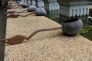 Coconut shell ladle in Thai native style is on brown floor beside pond, Thailand. Handle made from wood.