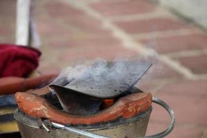 Clay fire pot with iron plow plate is on, smoke over plow and blur brick background, smoke above plow plate. Preparation equipment set for Thai massage in Northern style. photo