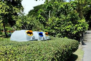 Row of plastic bins behind bush trees and beside concreate street in park. Three bins are used for waste separation in Bangkok, Thailand. photo