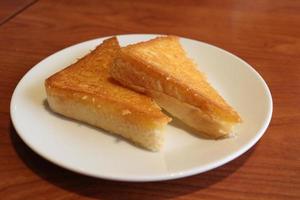 Two pieces of toasted triangle shape breads are on white round dish,The dish is on brown wood table.