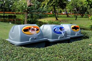 Row of plastic bins behind bush trees in park. Three bins are used for waste separation in Bangkok, Thailand. photo