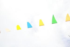 Yellow, blue, green flags in triangle shape are on thread and white sky background. photo