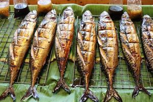 Saba fishes grilled are on stainless steel grate above banana leaves for sale with sauce, Thailand. photo