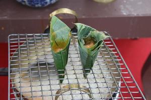 Two banana leaf cones are on stainless grate over syrup pan, red yolk in banana leaf cone is dropping into syrup, Thailand. Making Thai dessert Kai Mang Da. photo