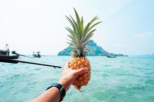 piña de verano, piña en mano en un barco en el mar foto