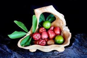 Citrus fruits and guava with leaves in wooden containers, black background