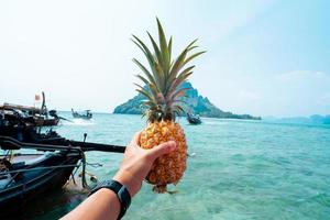 piña de verano, piña en mano en un barco en el mar foto