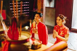 feliz joven pareja asiática con vestidos tradicionales chinos rezando en el templo foto