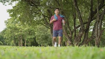 Asian old age man stop and resting during running at the park, standing under trees and rest after exercising, body wellness tired exhausted, men heath, elderly retired life, afternoon cardio wortout video