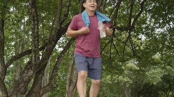 homem asiático de meia-idade correndo e descansando no parque, debaixo de árvores e descanso após o exercício, bem-estar corporal cansado exausto, cuidados de saúde masculinos, plano de seguro de vida, rotina de exercícios