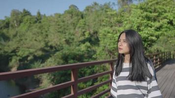 una joven turista activa gira alrededor del cuerpo caminando sobre un puente de madera que cruza el río dentro del parque nacional, relajante actividad de senderismo, fondo de follaje natural, cabello lacio que fluye hacia el viento video