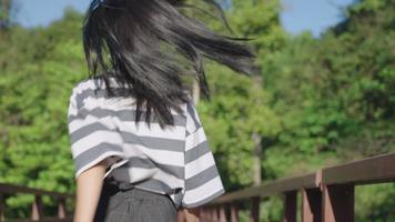 Rückansicht Low Angle Shot auf dem Rücken einer jungen, fröhlichen Frau, die auf einer Holzbrücke läuft, mit einem seidigen Haar, das in der Luft vorbeibläst, gesundes, glänzendes schwarzes Haar, Laufstrecke, grüne natürliche Erfrischung video