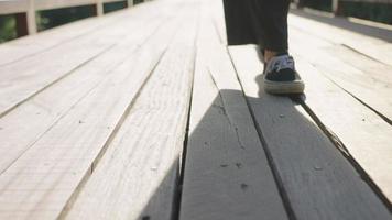Low Angle Shot auf einem Sneaker Füße zu Fuß auf der Holzbrücke, um einen Fluss im Nationalpark zu überqueren, schlendernde Geste, ein Silhouette menschlicher Schatten auf der Brücke, Wandern in grüner Umgebung video