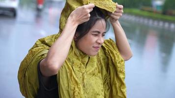 menina asiática usar capa de chuva amarela correndo colocar o capuz, começar a chover, clima de estação chuvosa chuva torrencial, má sorte se molhar enquanto sai para o trabalho, chuva na hora do rush, preso na chuva video