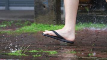 un pied de tongs courant sur le sentier pavé le jour de la pluie, sur la promenade du côté de la rue, rue inondée, avec pluie et eau, partie inférieure du corps, course pressée de trouver l'abri pour cacher la pluie video