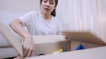 junge asiatische frau, die kleine kartonpaketzustellung öffnet, weibliche empfängerin packt kartonpaketbehälter aus, liefert lieferung, umzug in neue wohnung, lagerboxraum an neuem ort video
