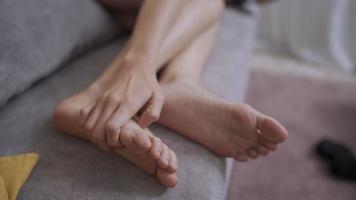 Close up shot of young female hand massage and scratch her foot, model lying  down on gray sofa try to relaxing at home, allergy dust, muscle stress discomfort , light skin barefoot, muscle pain cramp video